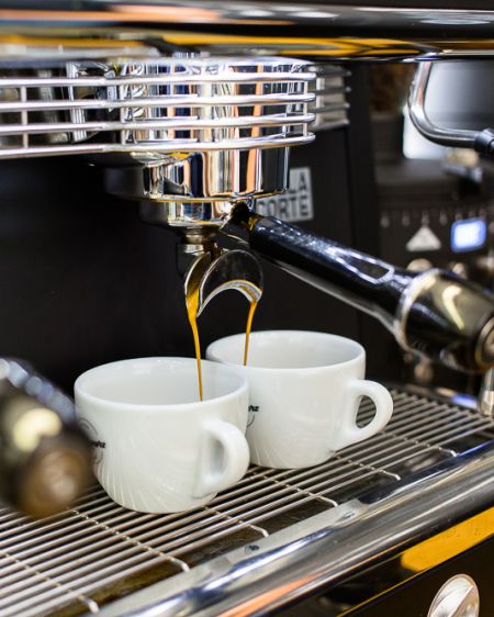 Zwei weiße Kaffeetassen stehen unter einer Siebträgermaschine, während Kaffee in die beiden Tassen fließt