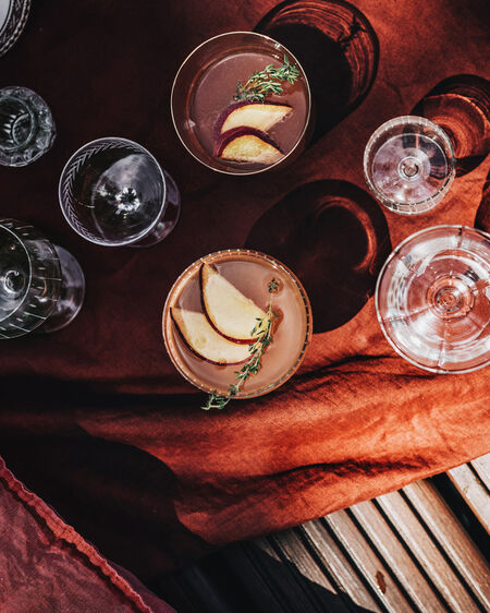 KPM Gläser, zwei davon mit einem Pfirsich-Sommer-Drink gefüllt, auf rostfarbener Picknickdecke auf Steg