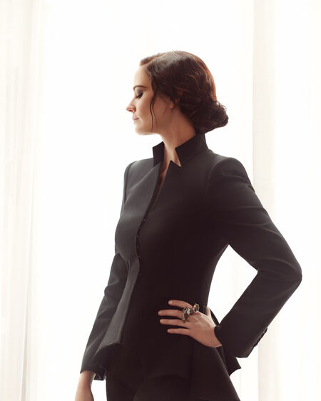 Eva Green in schwarzem Hosenanzug steht vor Fenster mit bodenlangen Vorhängen