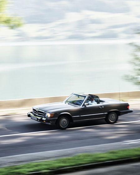 Oldtimer-Cabrio fährt auf Landstraße am See entlang