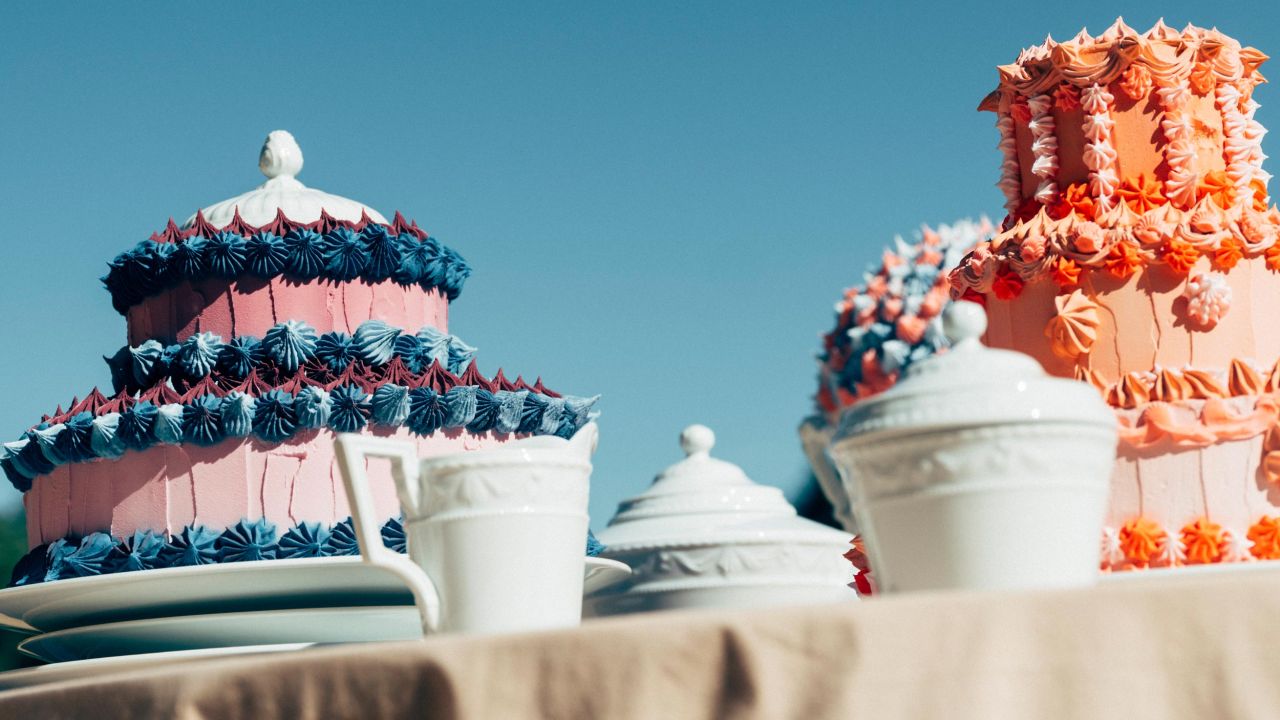 Two large, elaborately decorated cakes and KPM porcelain on a table outdoors under a blue sky Two large, elaborately decorated cakes and KPM porcelain on a table outdoors under a blue sky