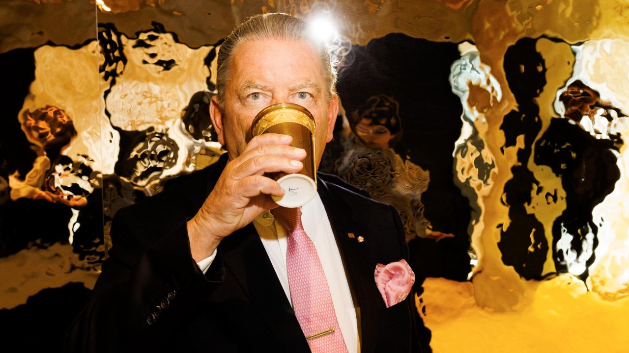 Close-up of a man in a suit and tie drinking from a golden cup, with a highly reflective golden wall in the background Close-up of a man in a suit and tie drinking from a golden cup, with a highly reflective golden wall in the background