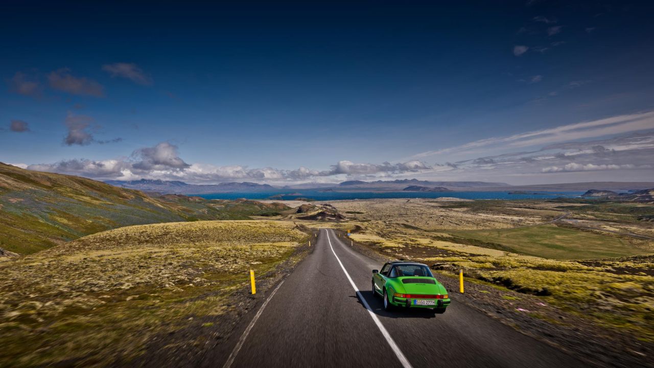 A green vintage Porsche drives along an empty country road through a mountainous landscape in Iceland. A green vintage Porsche drives along an empty country road through a mountainous landscape in Iceland.
