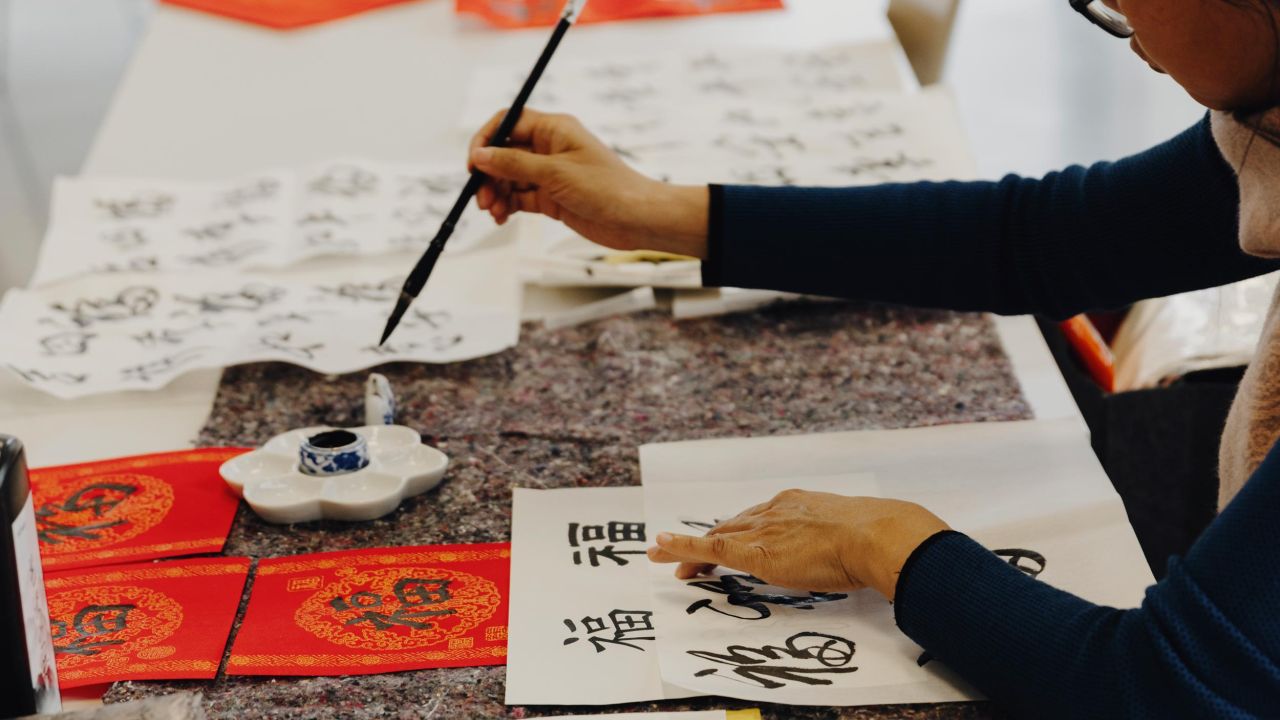 Woman sitting at a table writing Chinese characters with a brush on a white sheet of paper Woman sitting at a table writing Chinese characters with a brush on a white sheet of paper