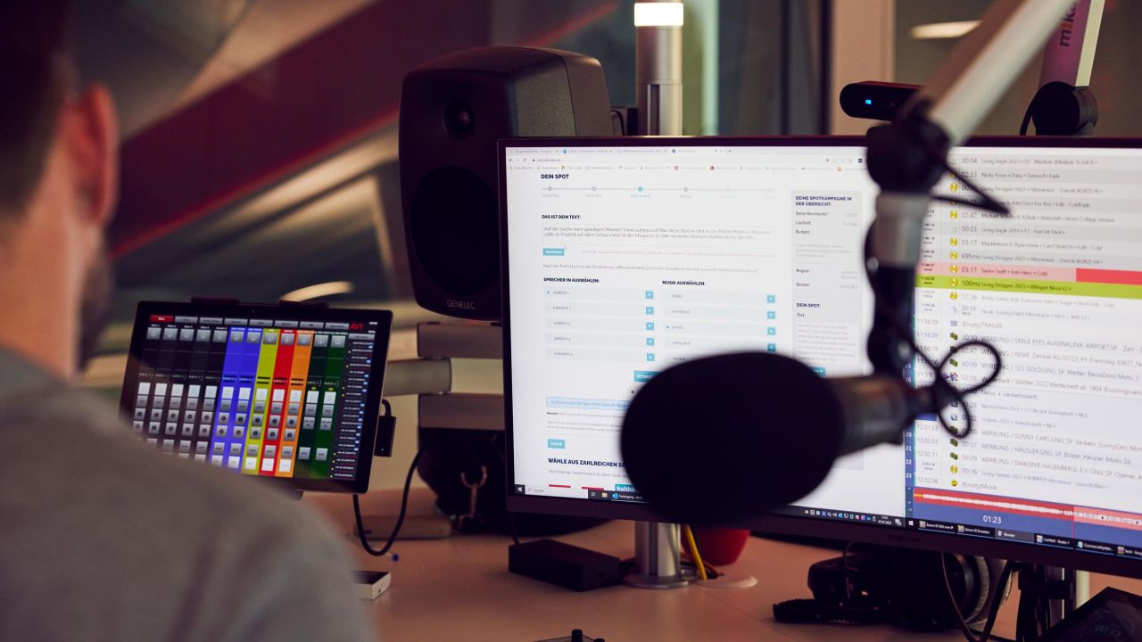 Ansicht über die Schulter eines Mannes in einem Radiostudio, der auf mehrere Monitore blickt, die Steuerungsoberflächen und Produktions-Timelines anzeigen Ansicht über die Schulter eines Mannes in einem Radiostudio, der auf mehrere Monitore blickt, die Steuerungsoberflächen und Produktions-Timelines anzeigen